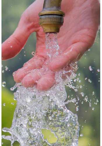 Mano tocando agua corriendo en una fuente.
